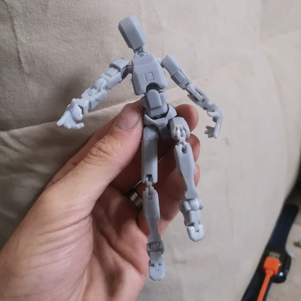 A grey articulated robot held in a hand against a light background, showing its arm, leg and torso segments.