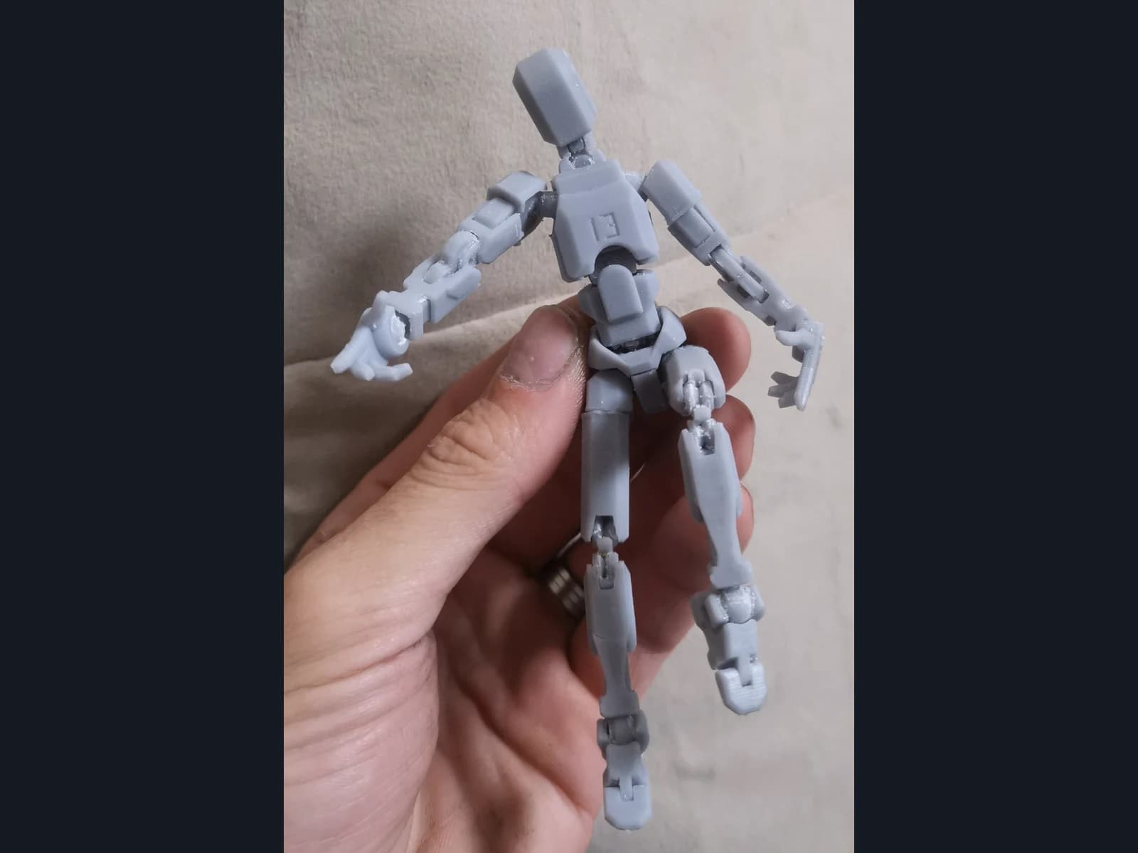 A grey articulated robot held in a hand against a light background, showing its arm, leg and torso segments.