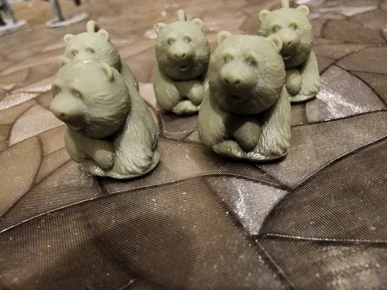 Five grey-green bear figurines with loops on a patterned surface.