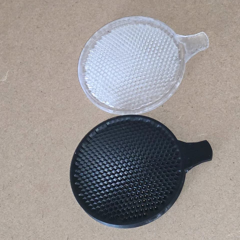 Pale and black circular mesh parts with side tabs on a beige surface.
