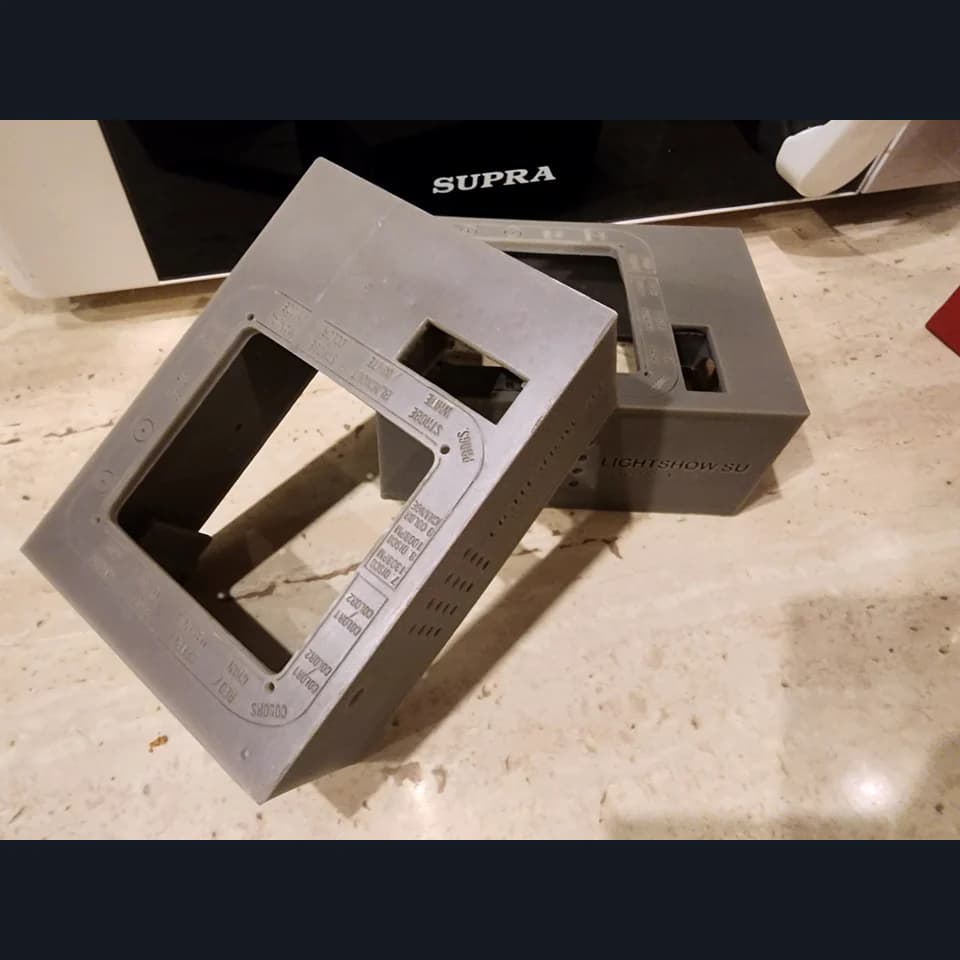 Two grey control panel enclosures with rectangular openings, labels and side holes on a work surface.