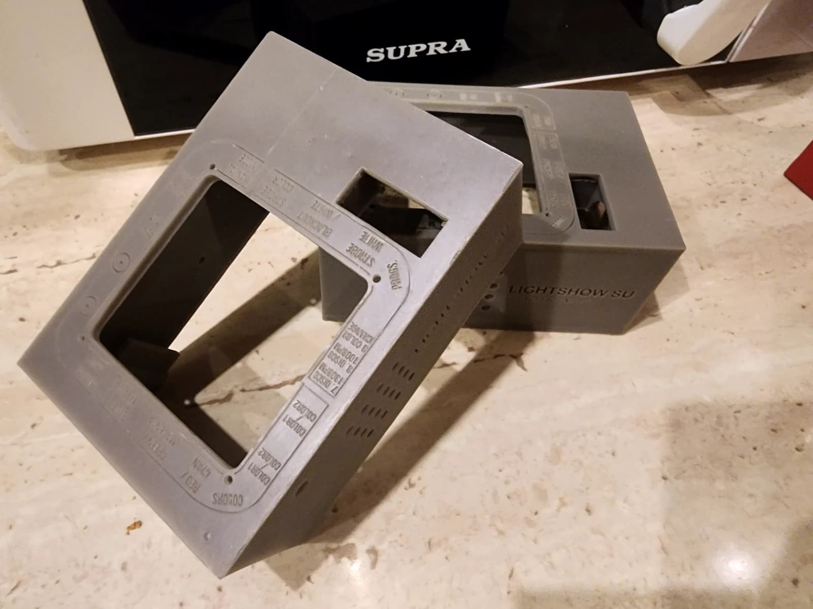 Two grey control panel enclosures with rectangular openings, labels and side holes on a work surface.