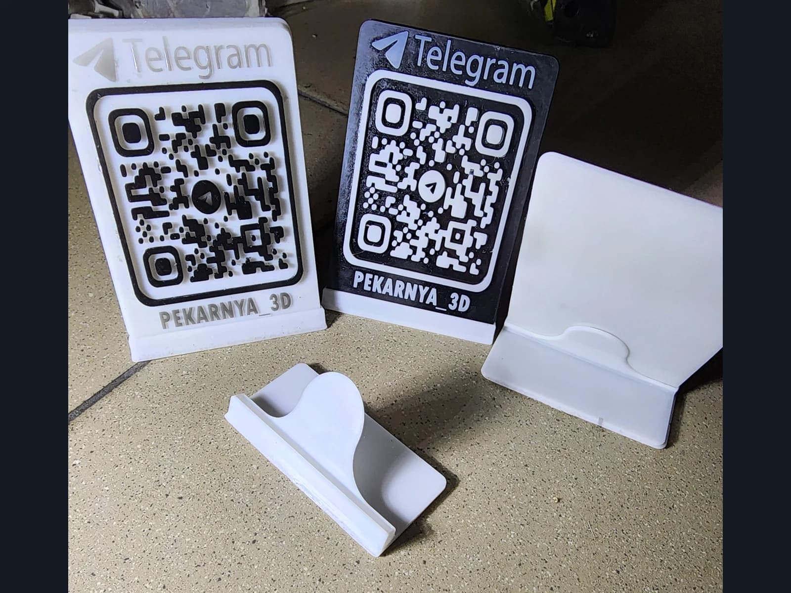 Light and dark QR signs with Telegram lettering, a white panel and a separate stand on a work surface.