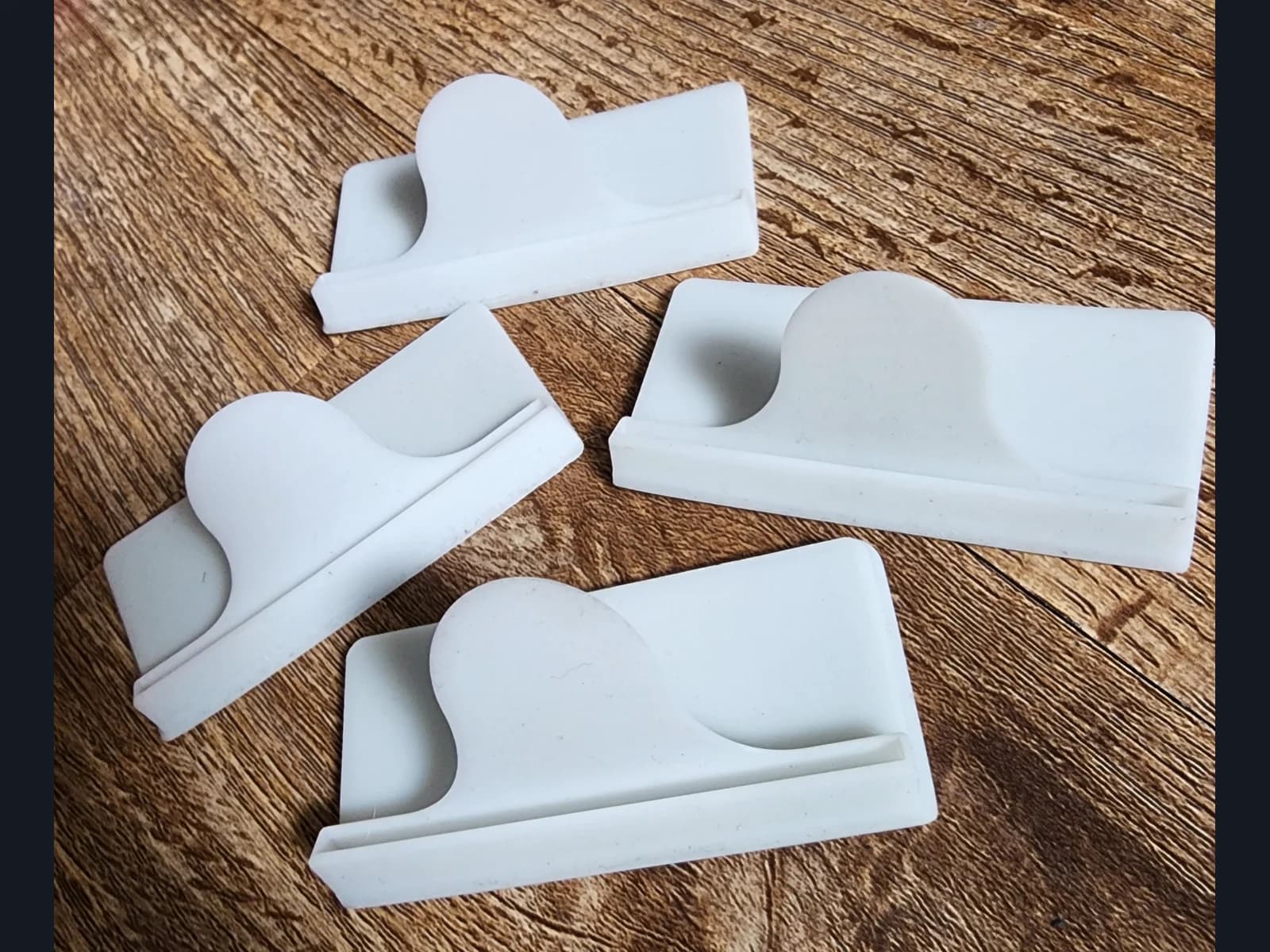 Four white holders with long slots and curved rear supports on a wooden surface.