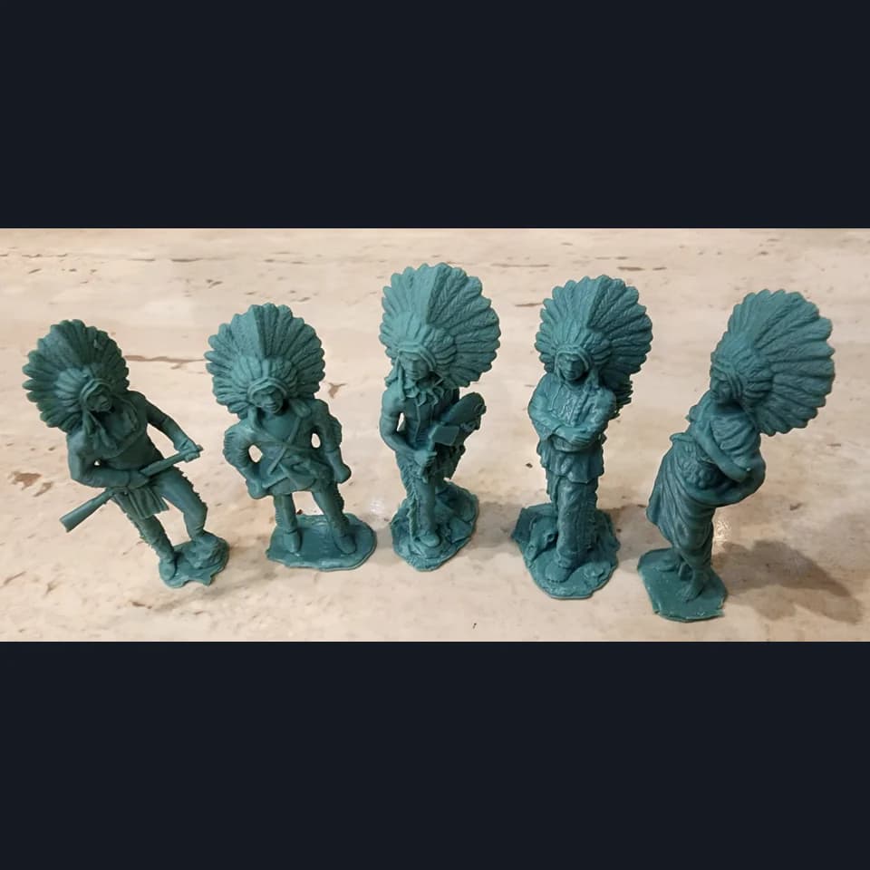 Five green miniatures in feather headdresses on a pale work surface.
