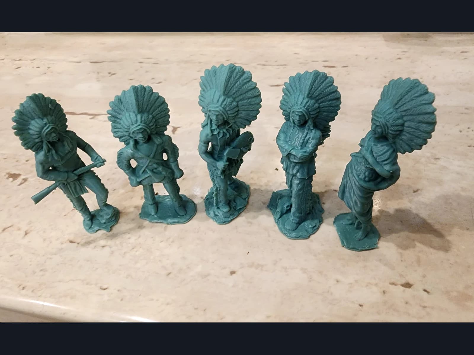 Five green miniatures in feather headdresses on a pale work surface.