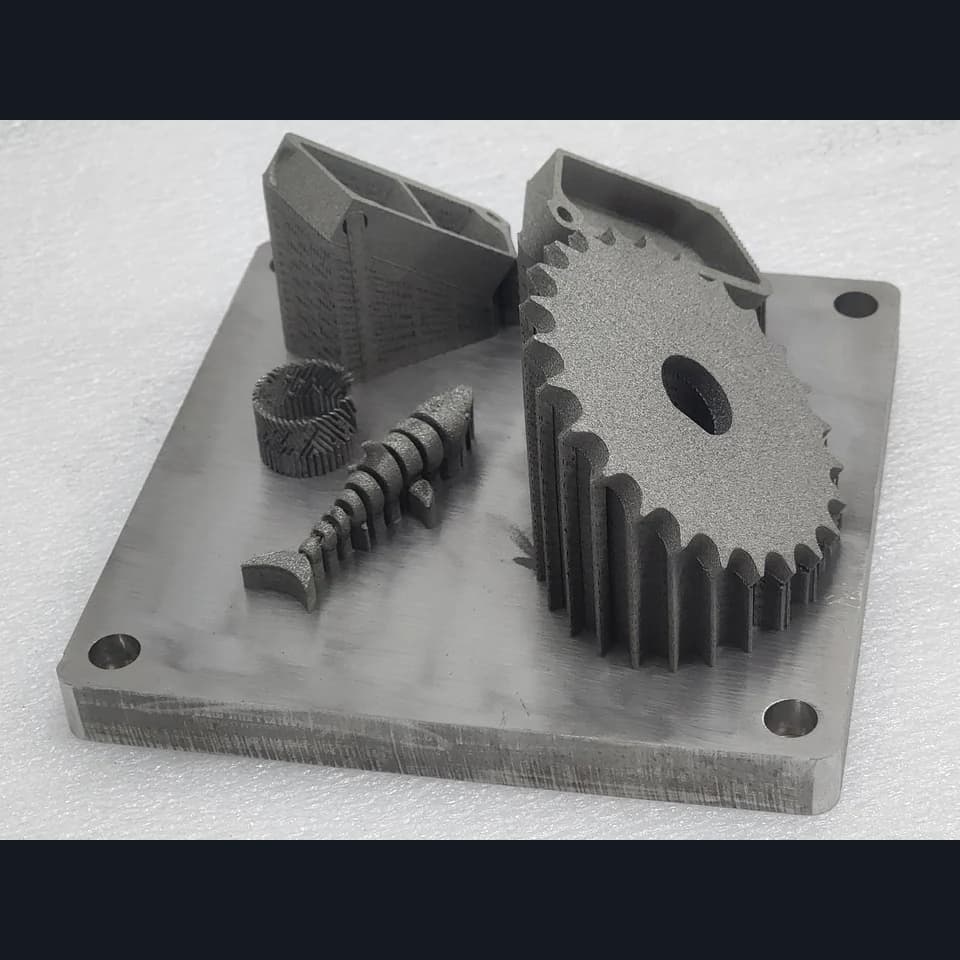 A gear with a central opening, a worm and small housing parts on a square build plate with mounting holes.