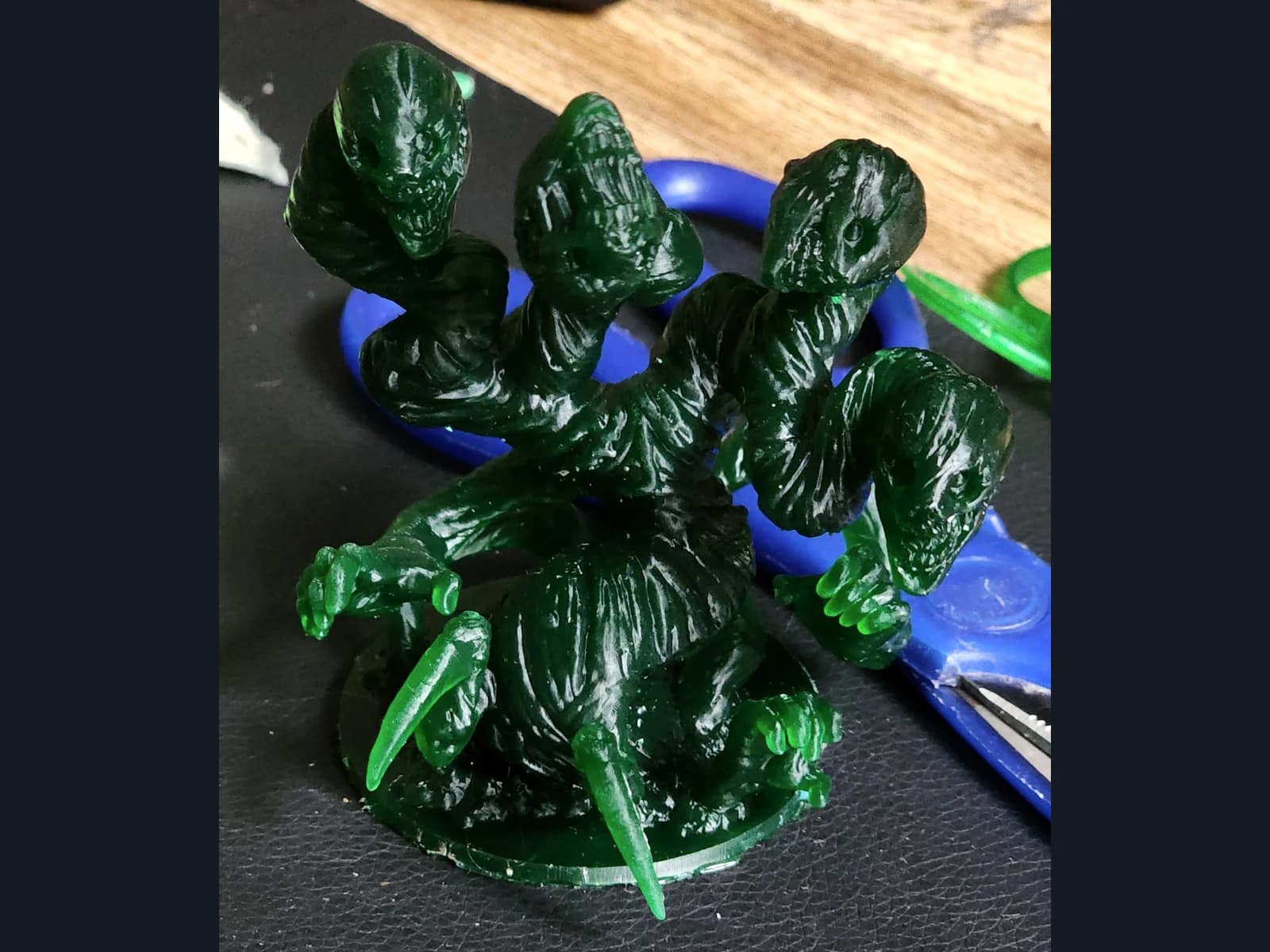 A translucent green multi-headed creature with claws on a round base, resting on a dark work surface.