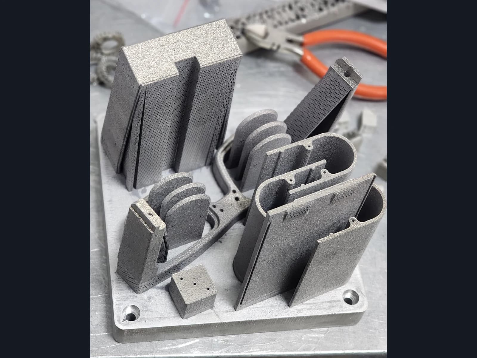 Grey housing elements and brackets with holes and supports on a shared build plate.