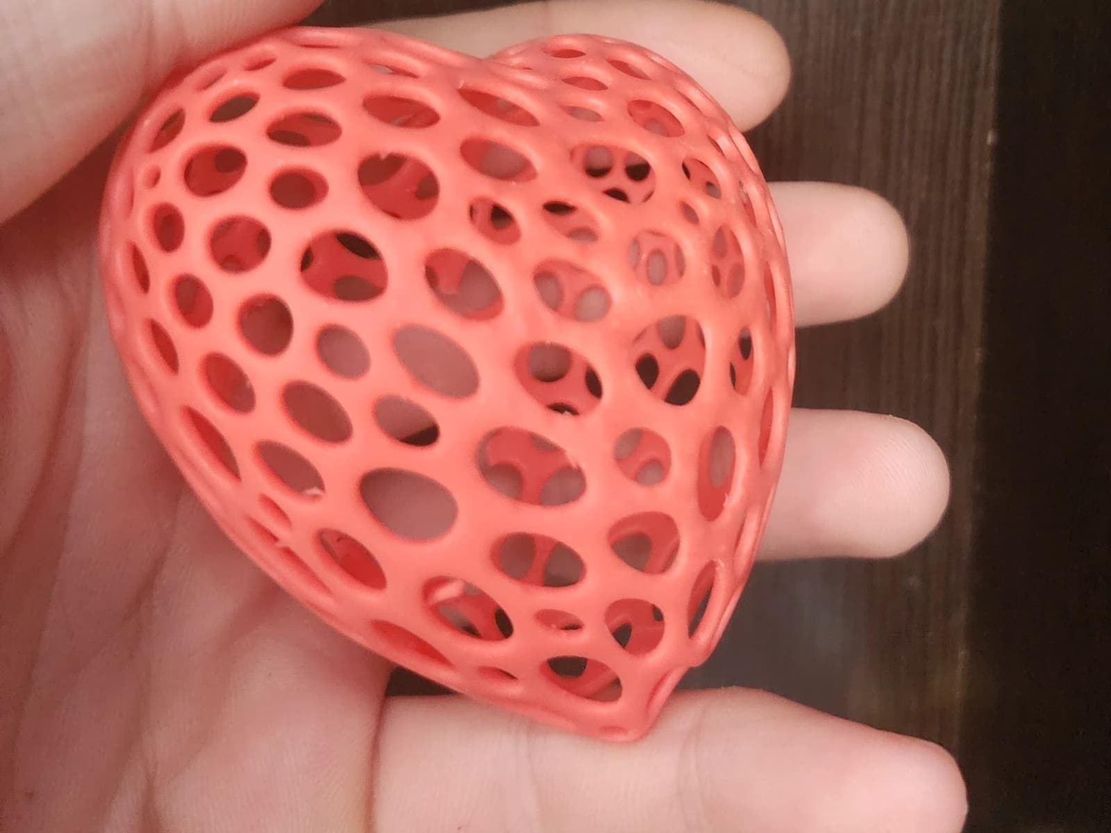 A coral-coloured three-dimensional heart with rounded openings resting on a palm.