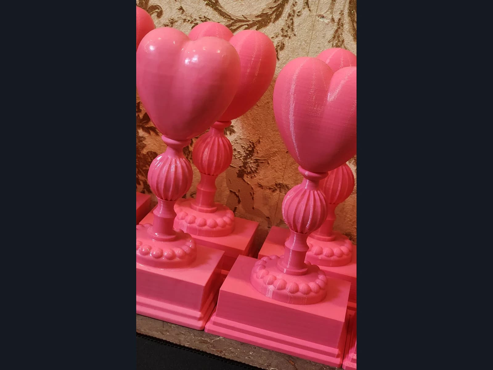 Pink decorative trophies with three-dimensional hearts, ribbed stems and stepped square bases, arranged next to each other.