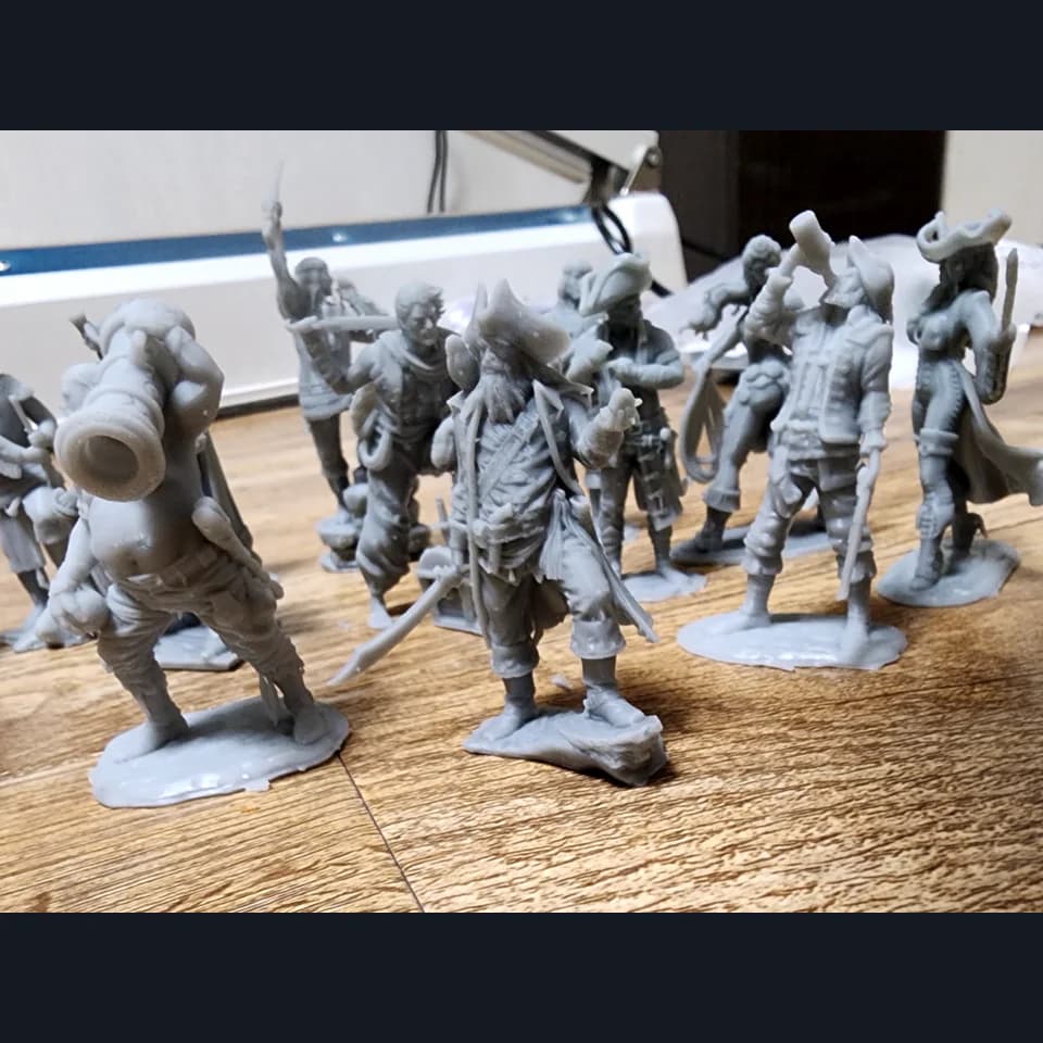 Grey pirate miniatures on individual bases, including figures in tricorn hats, with sabres and a cannon carried on a shoulder.
