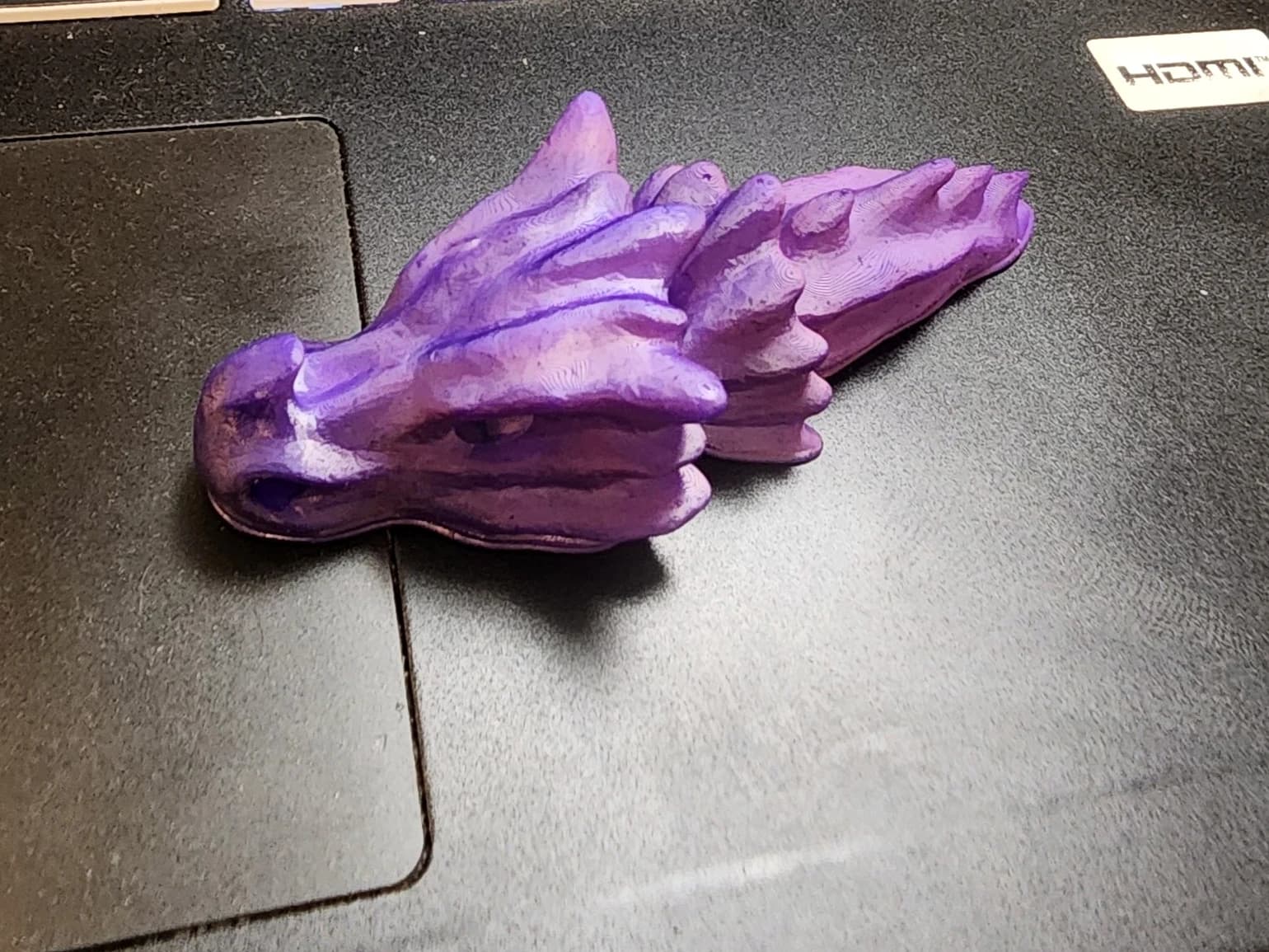 A purple dragon head with horns and sculpted ridges on the dark surface of a laptop.