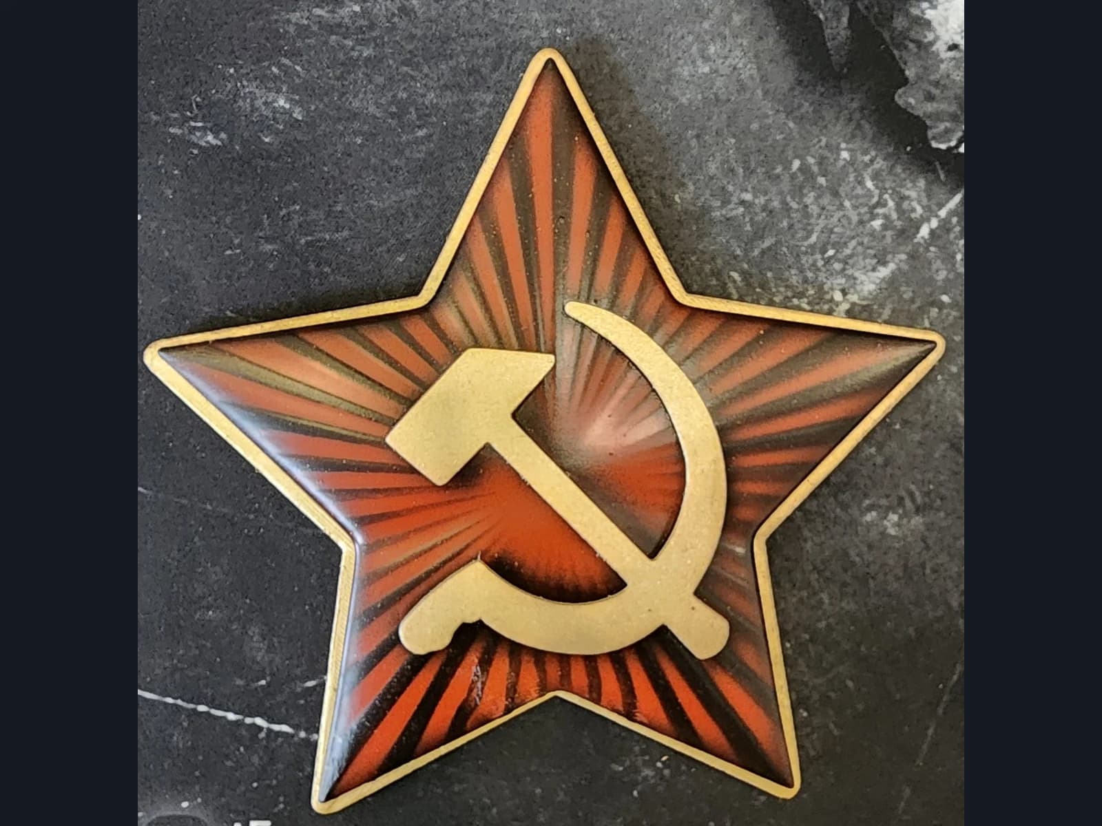 A decorative red star with a gold-coloured hammer, sickle and border on a dark surface.