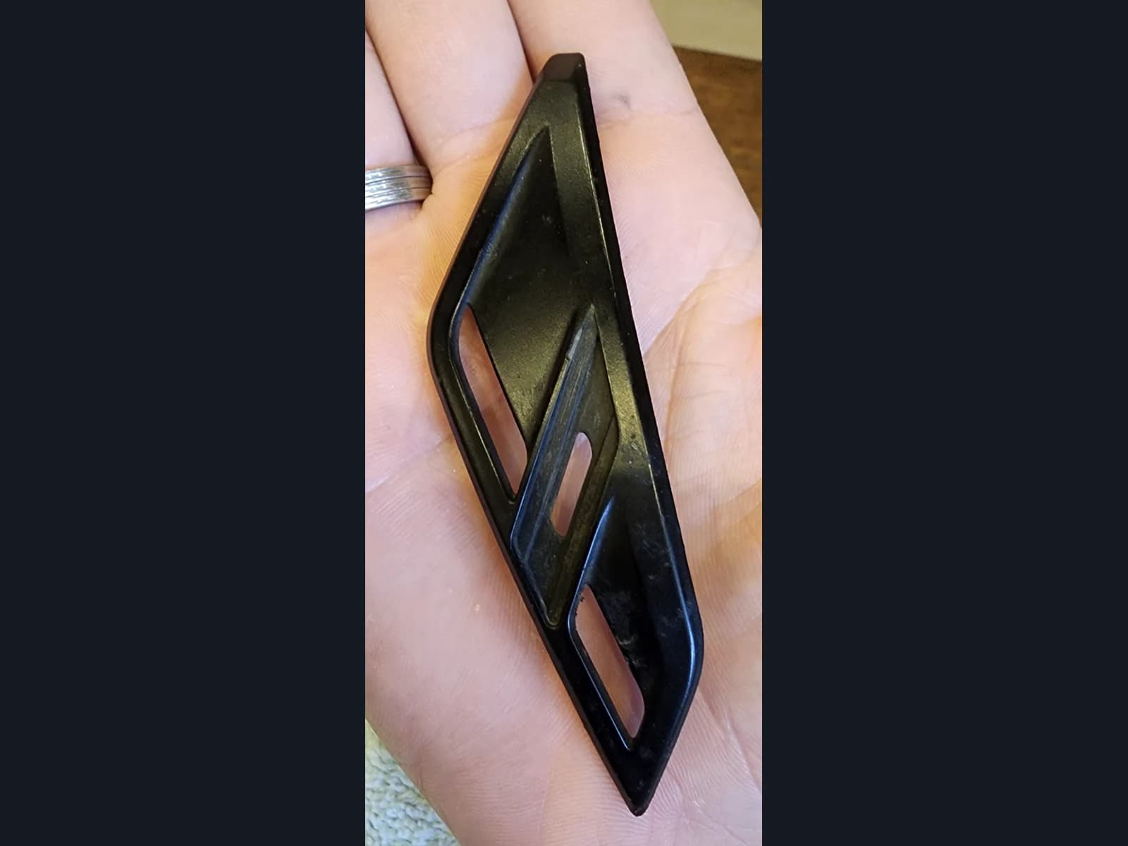 An elongated black trim piece with three slots resting on a palm.