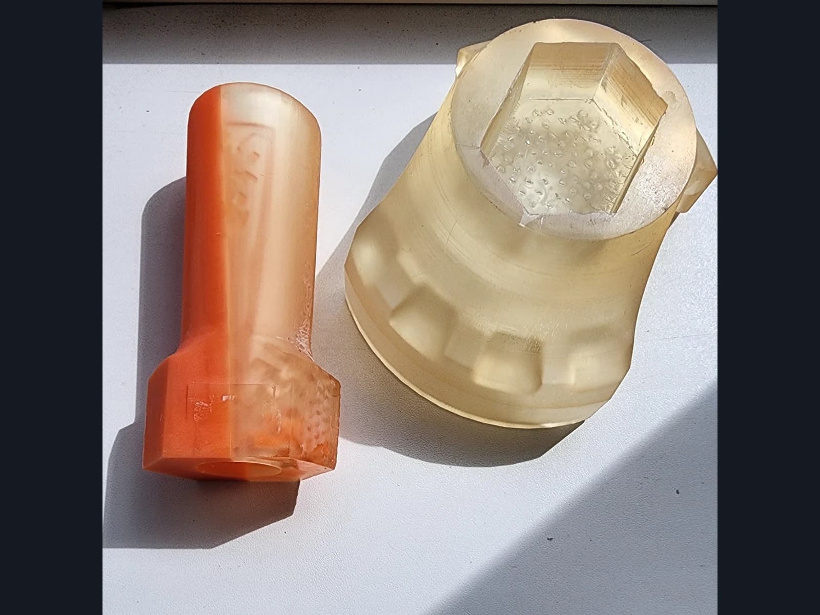 An orange cylindrical part and a wider pale part with a hexagonal recess on a white surface.