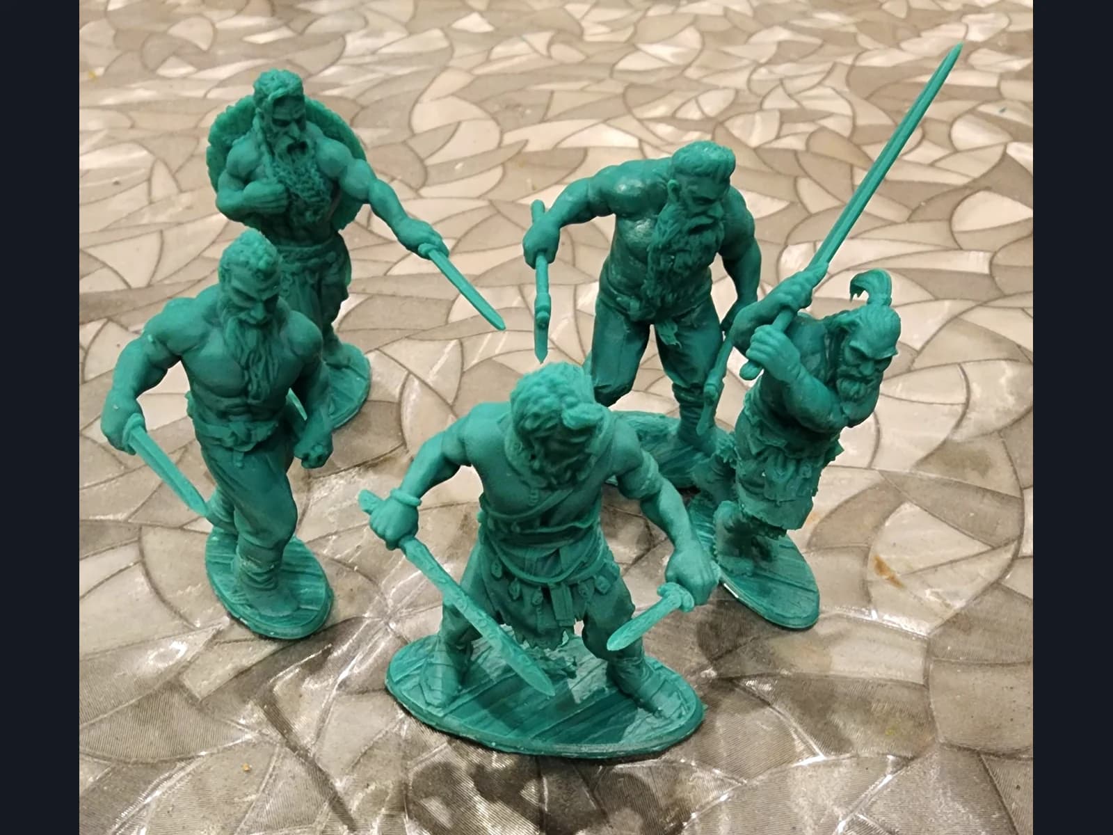 Five green warrior miniatures with swords and axes on textured bases, arranged on a work surface.