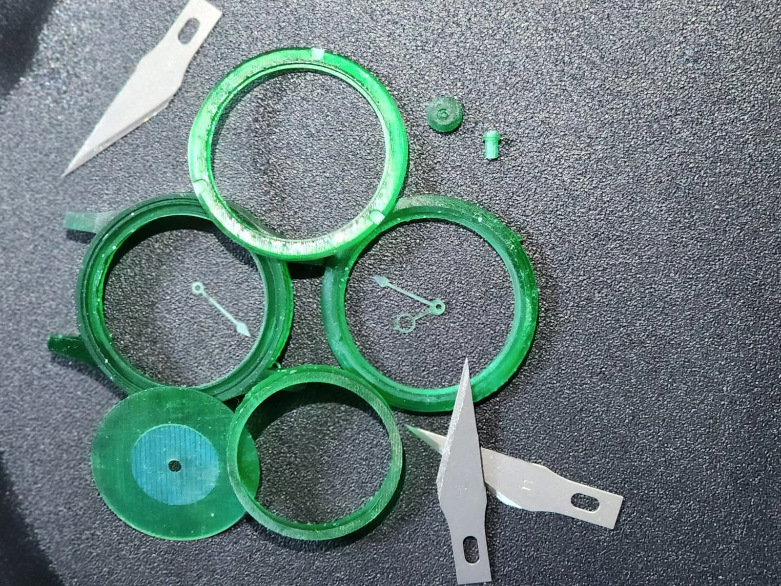 Green watch case rings, a circular insert and hands on a dark work surface.