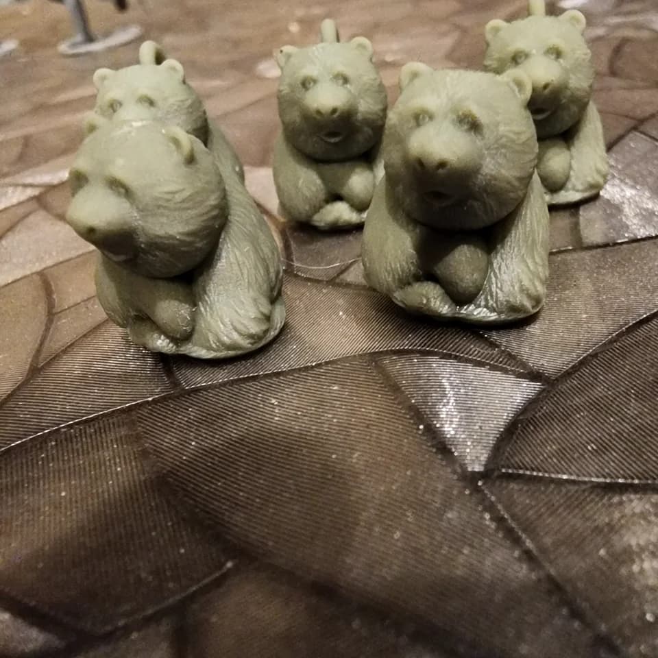 Five grey-green bear figurines with loops on a patterned surface.