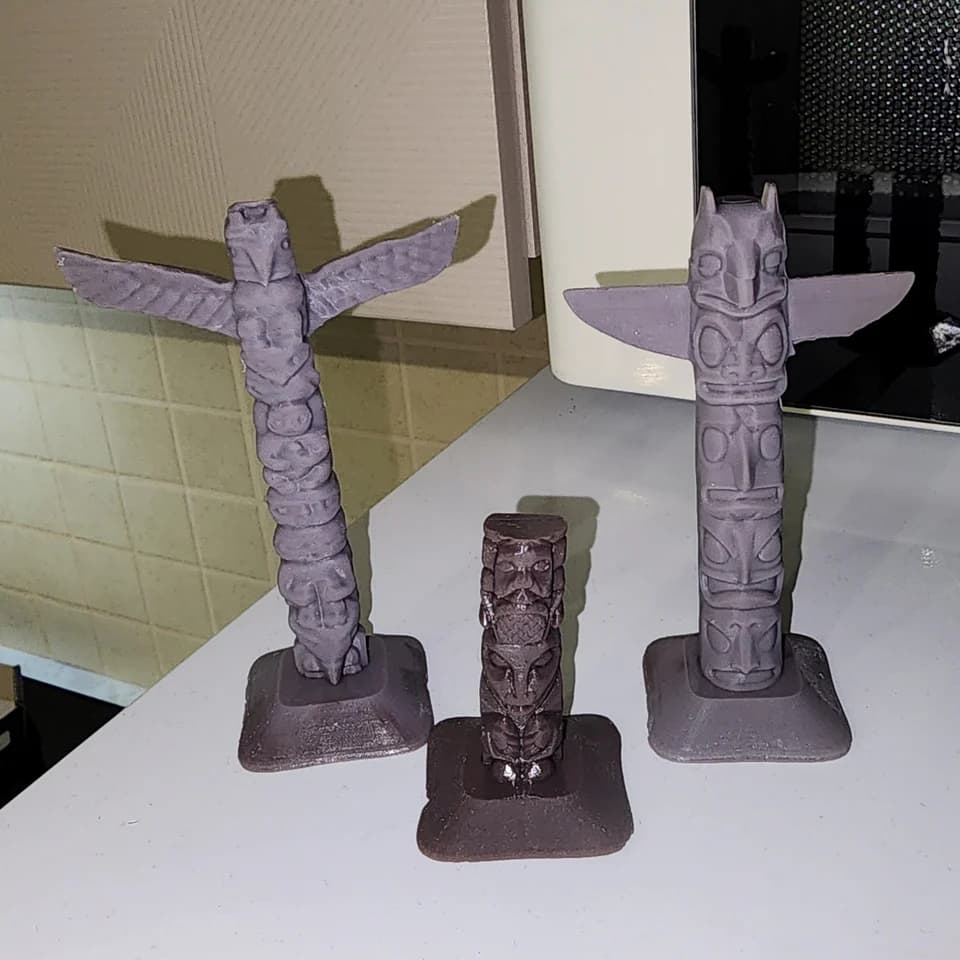 Three decorative poles on rectangular bases: two tall pieces with outstretched wings and one shorter piece, with raised faces along their surfaces.