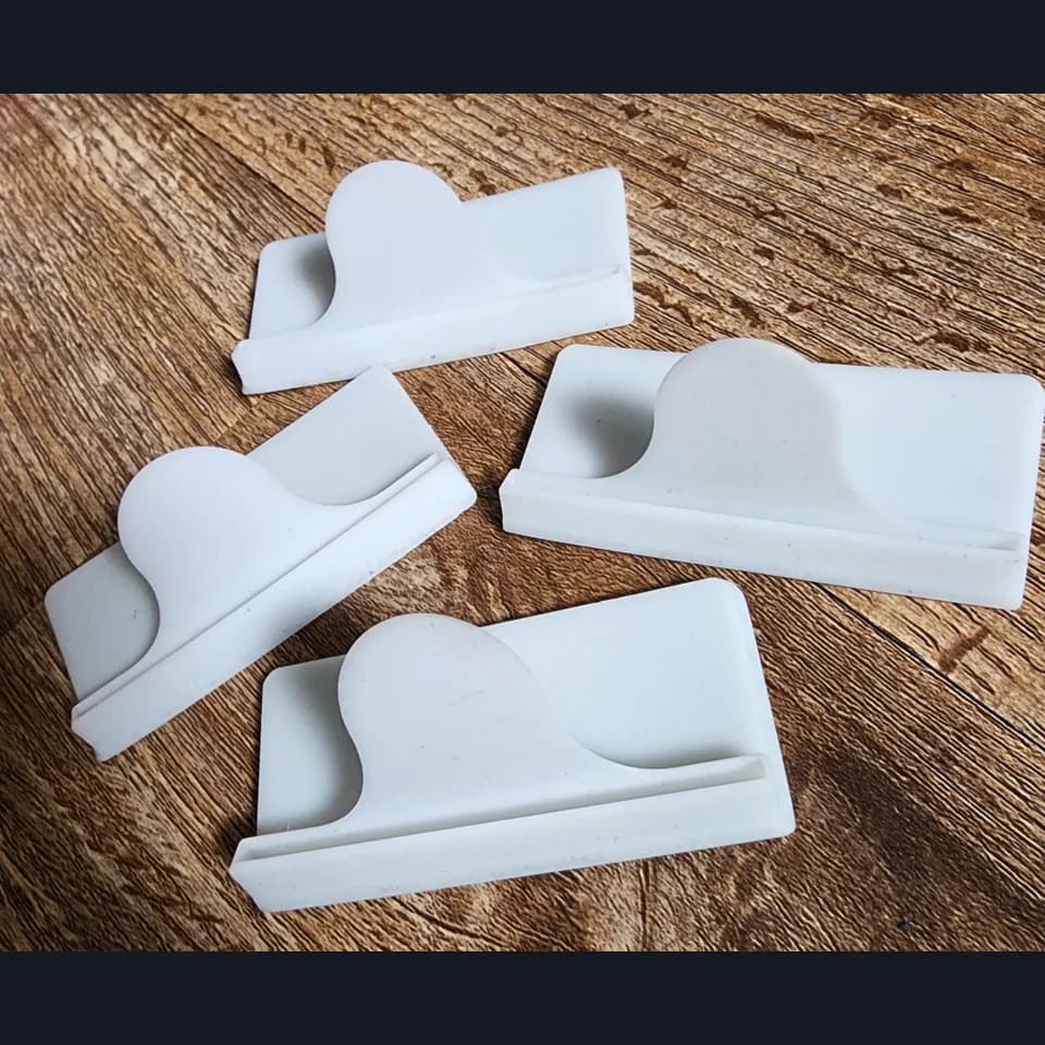 Four white holders with long slots and curved rear supports on a wooden surface.