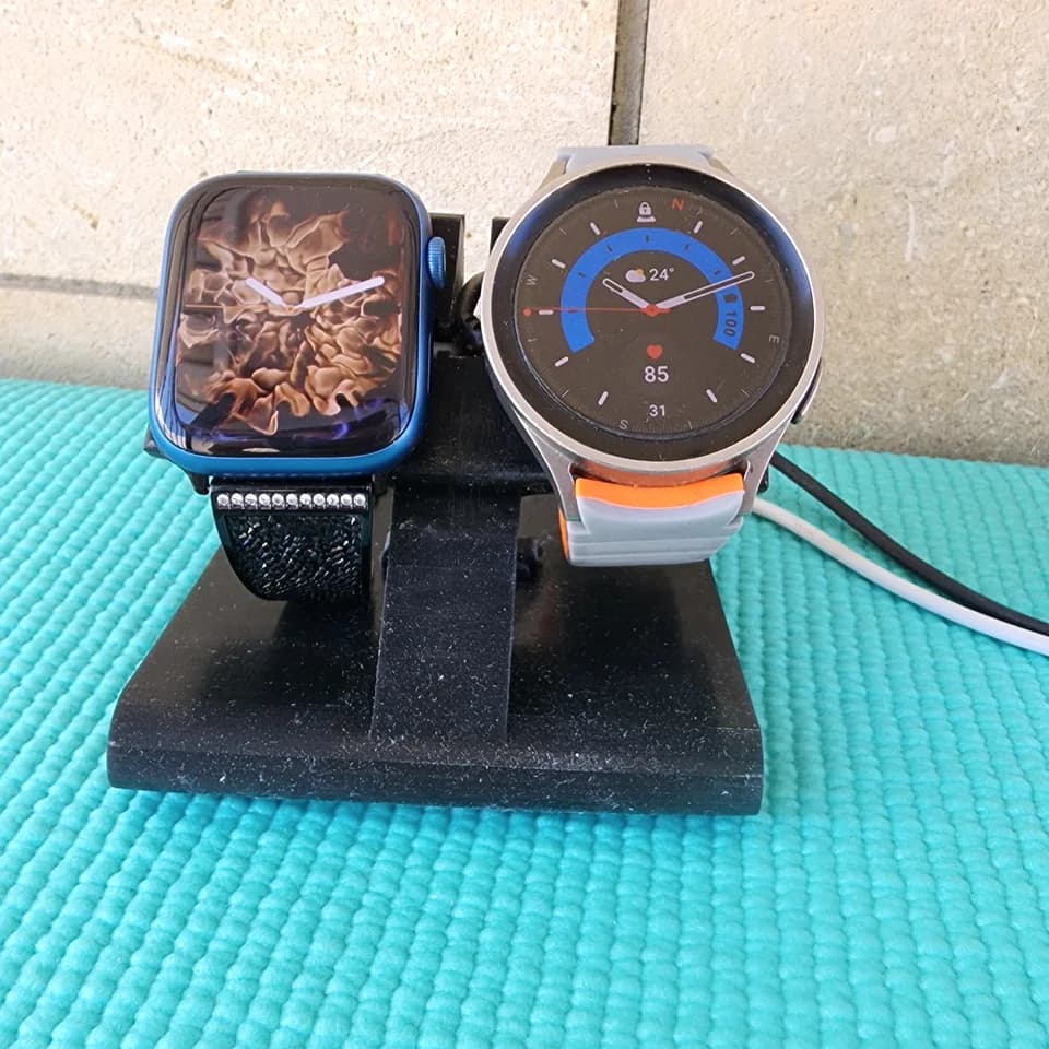 A black desktop stand holding two smartwatches on a turquoise surface.