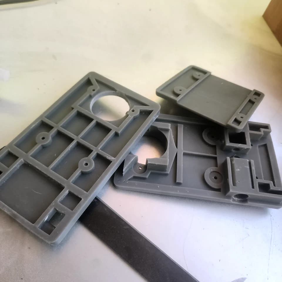 Grey enclosure panels with internal ribs, openings and mounting posts on a work surface.