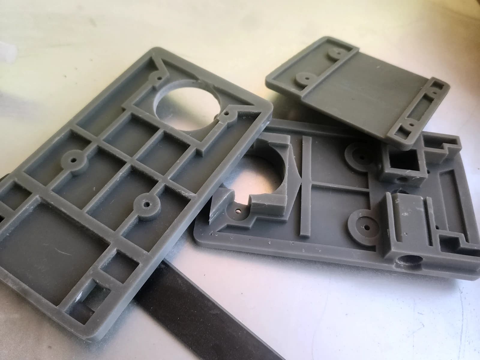 Grey enclosure panels with internal ribs, openings and mounting posts on a work surface.