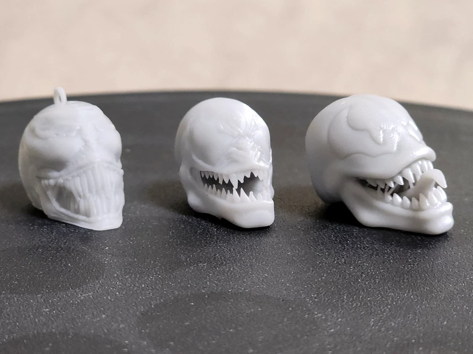 Three white fantasy skull pendants with detailed teeth on a dark surface.