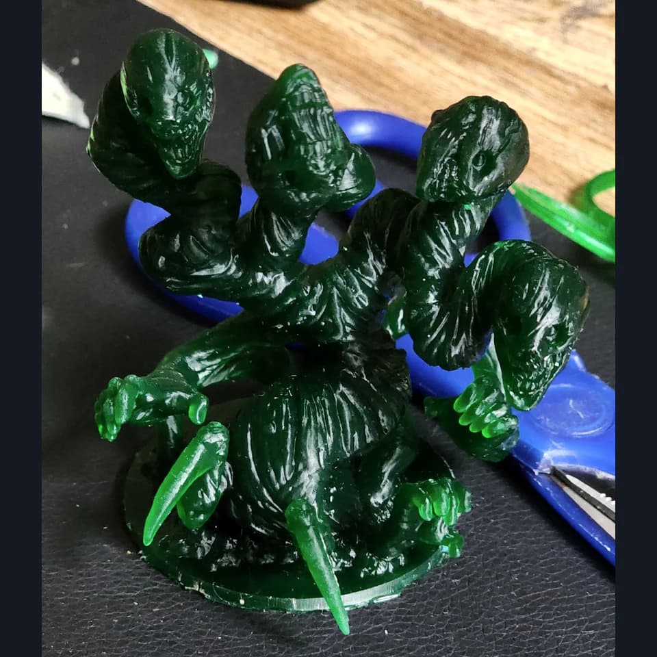 A translucent green multi-headed creature with claws on a round base, resting on a dark work surface.