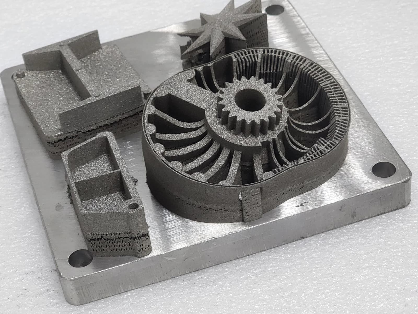 An impeller with curved blades and a toothed central hub beside housing parts on a build plate.