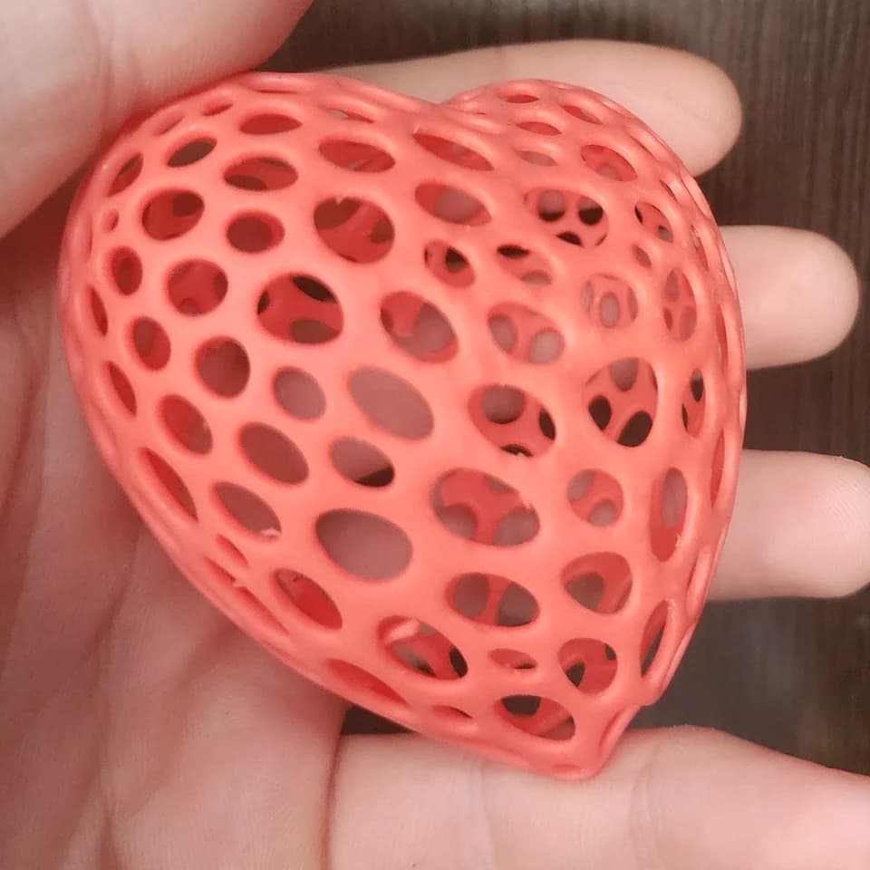 A coral-coloured three-dimensional heart with rounded openings resting on a palm.