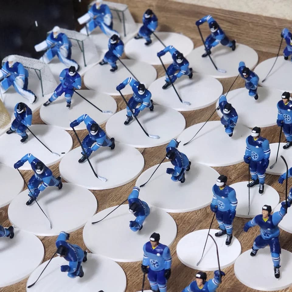Rows of painted hockey player miniatures in blue uniforms on white bases, with sticks and goals.