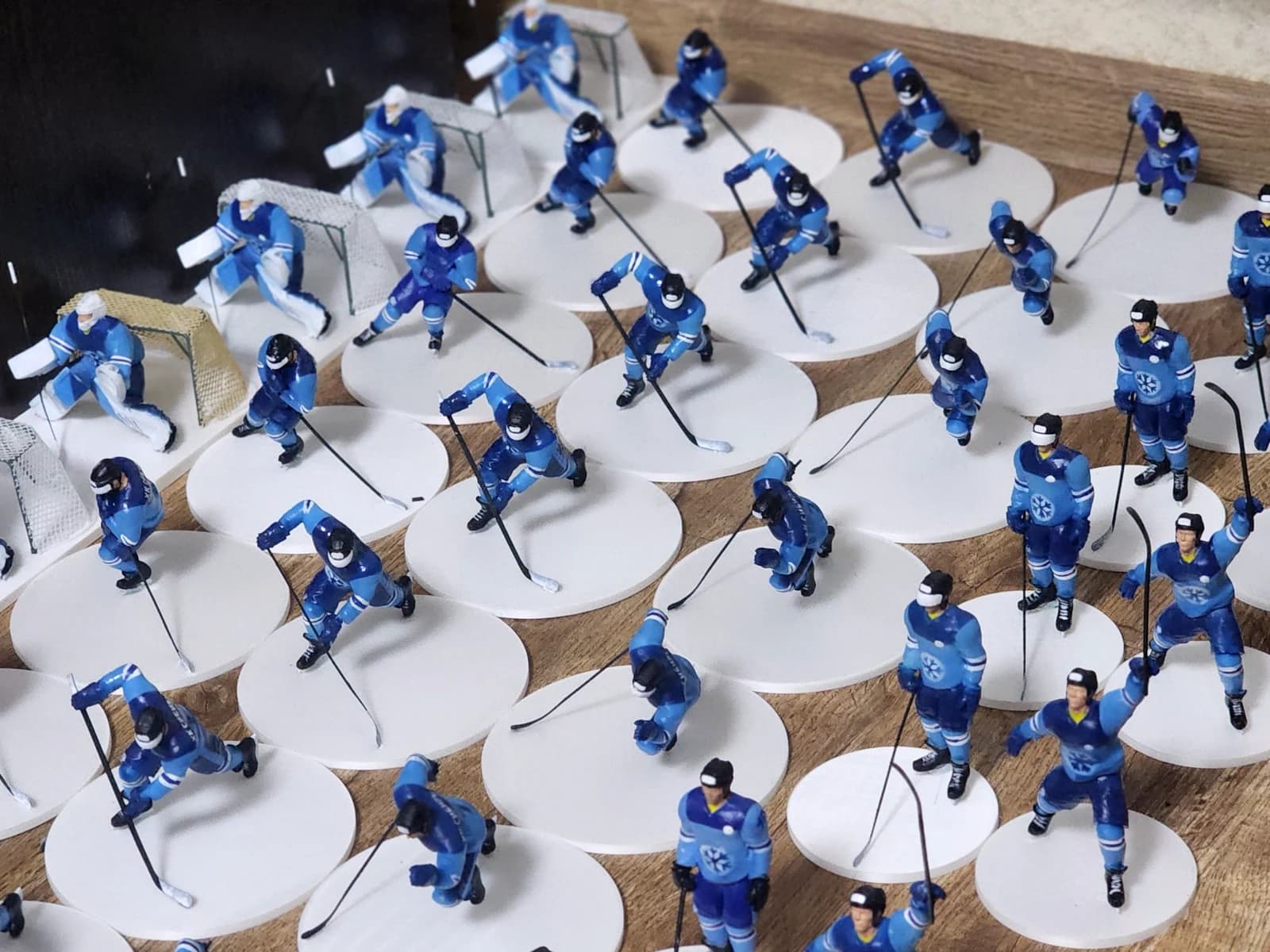 Rows of painted hockey player miniatures in blue uniforms on white bases, with sticks and goals.