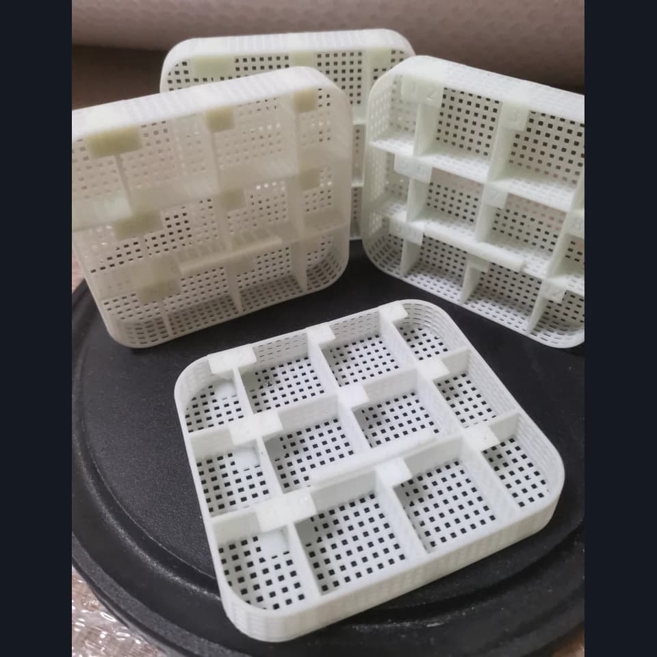 White perforated trays with internal dividers and tabs along their upper edges on a dark circular stand.