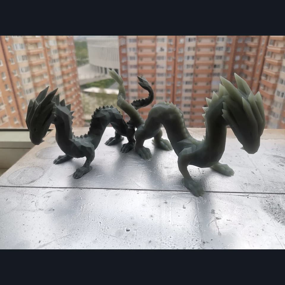 Two grey dragon figurines with faceted surfaces, curved necks and raised tails on a windowsill.
