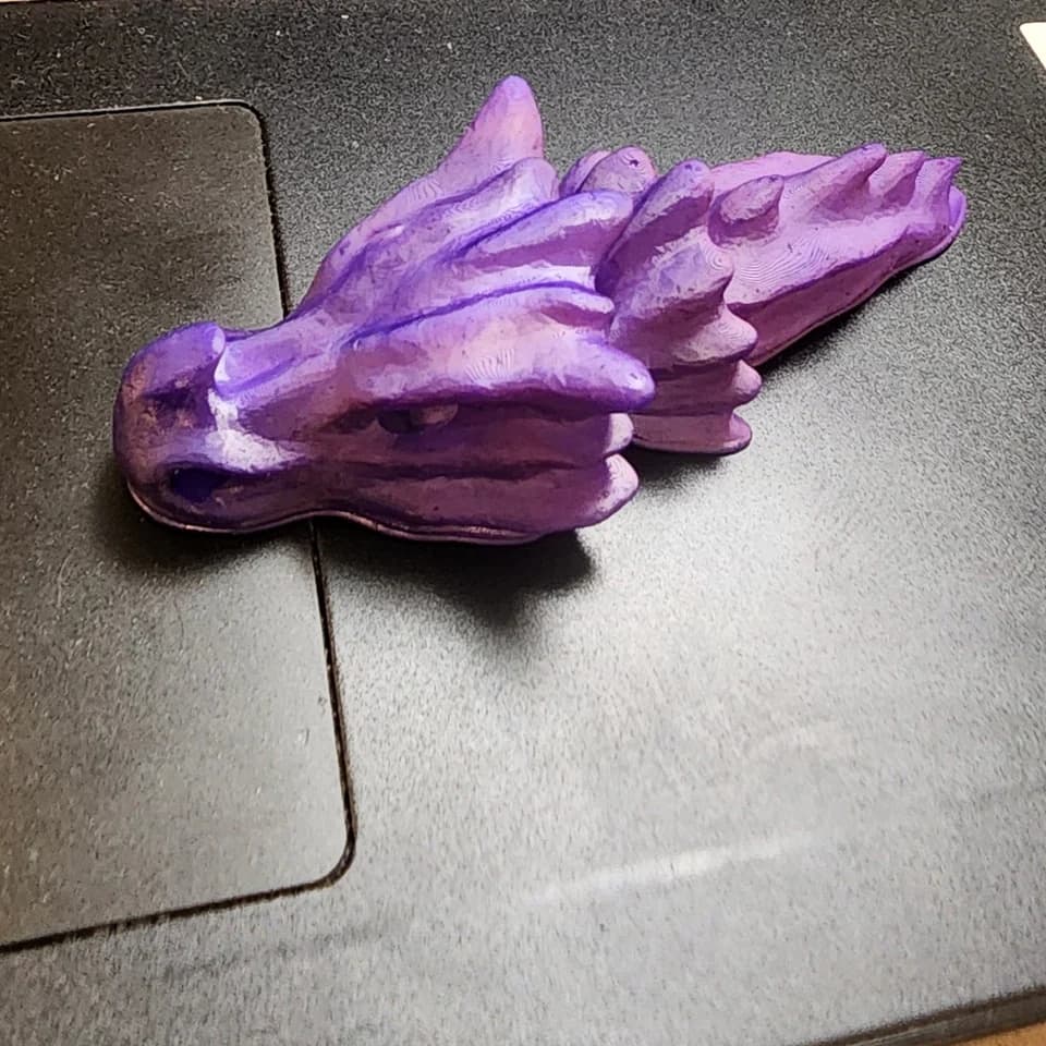 A purple dragon head with horns and sculpted ridges on the dark surface of a laptop.