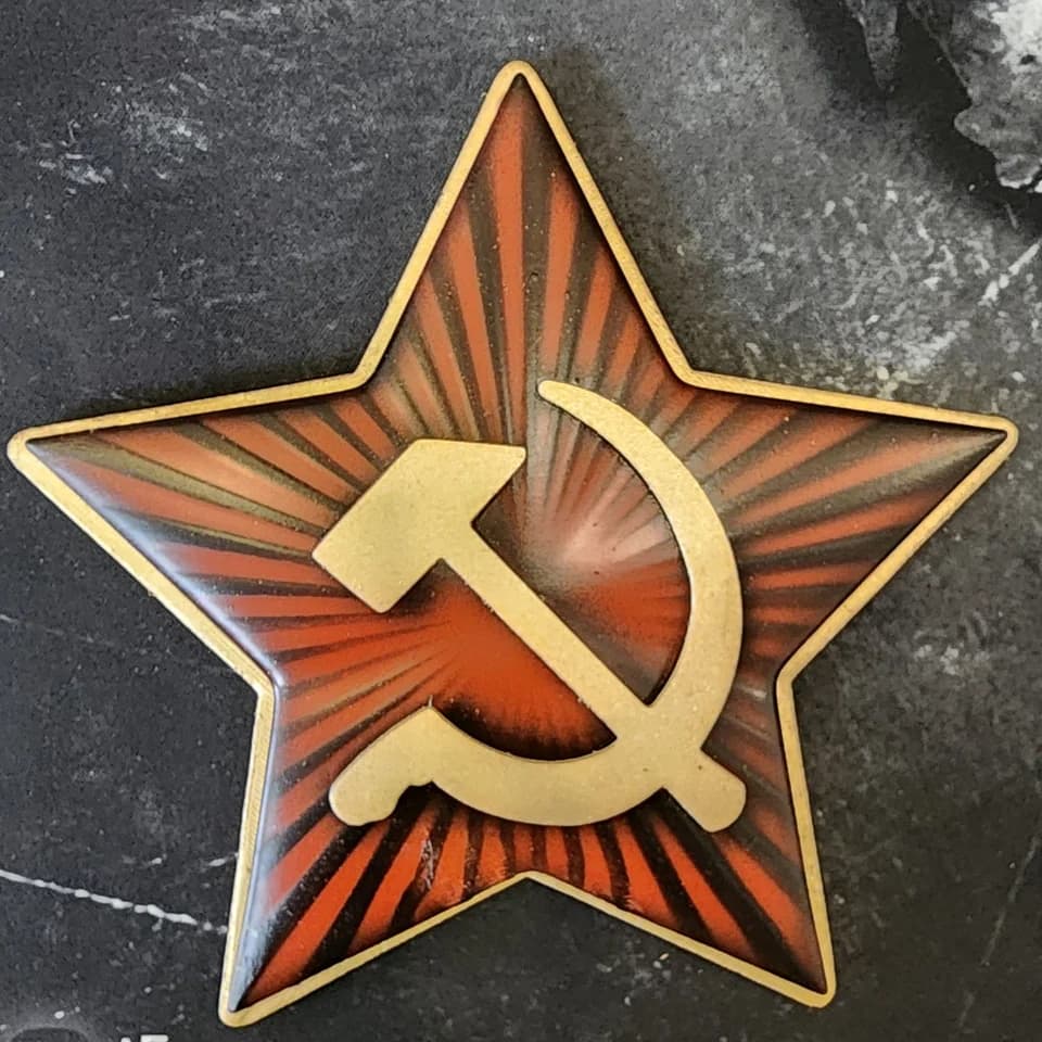 A decorative red star with a gold-coloured hammer, sickle and border on a dark surface.