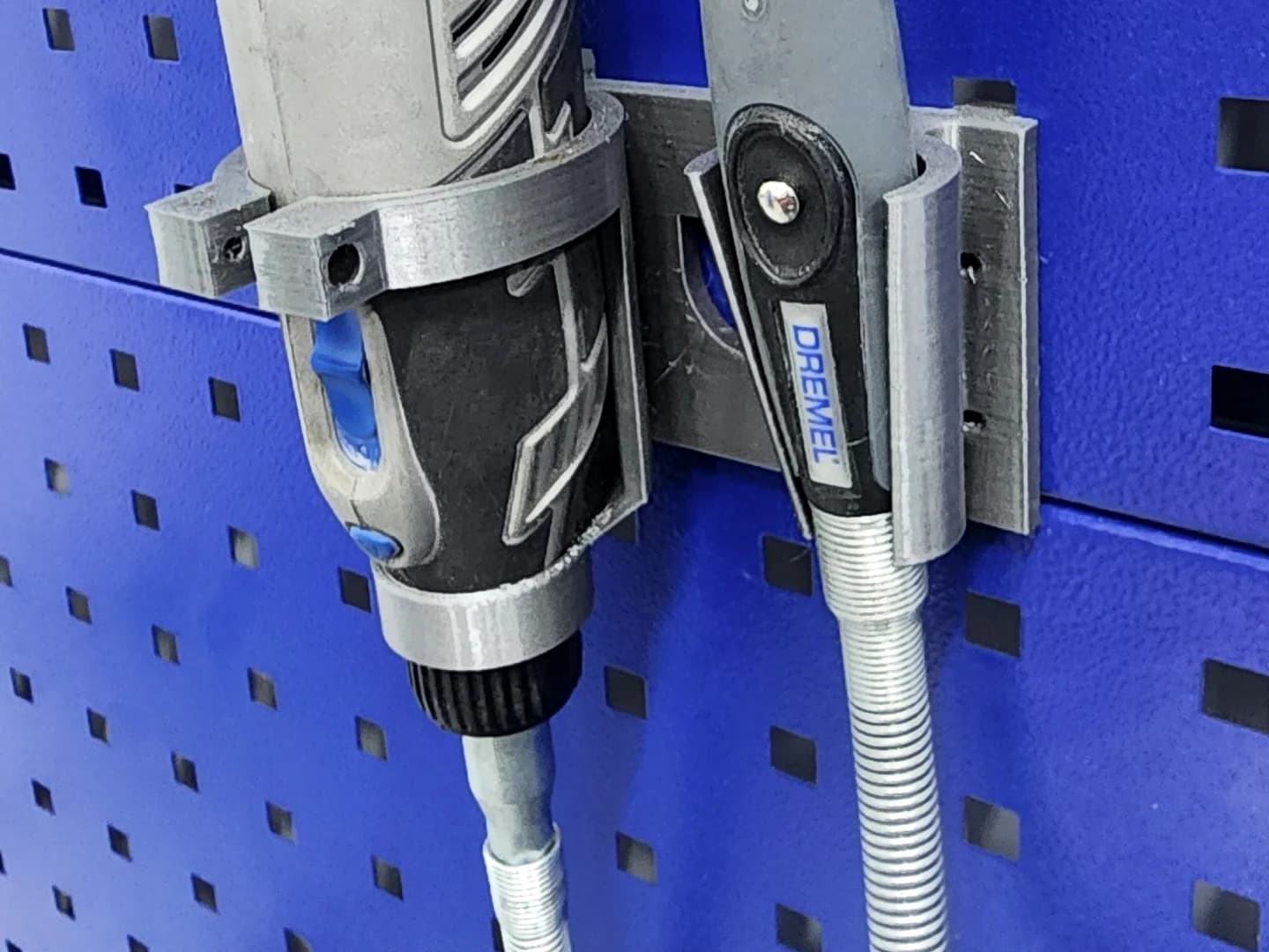 Grey holders for a rotary tool and flexible-shaft handpiece mounted on a blue perforated panel.