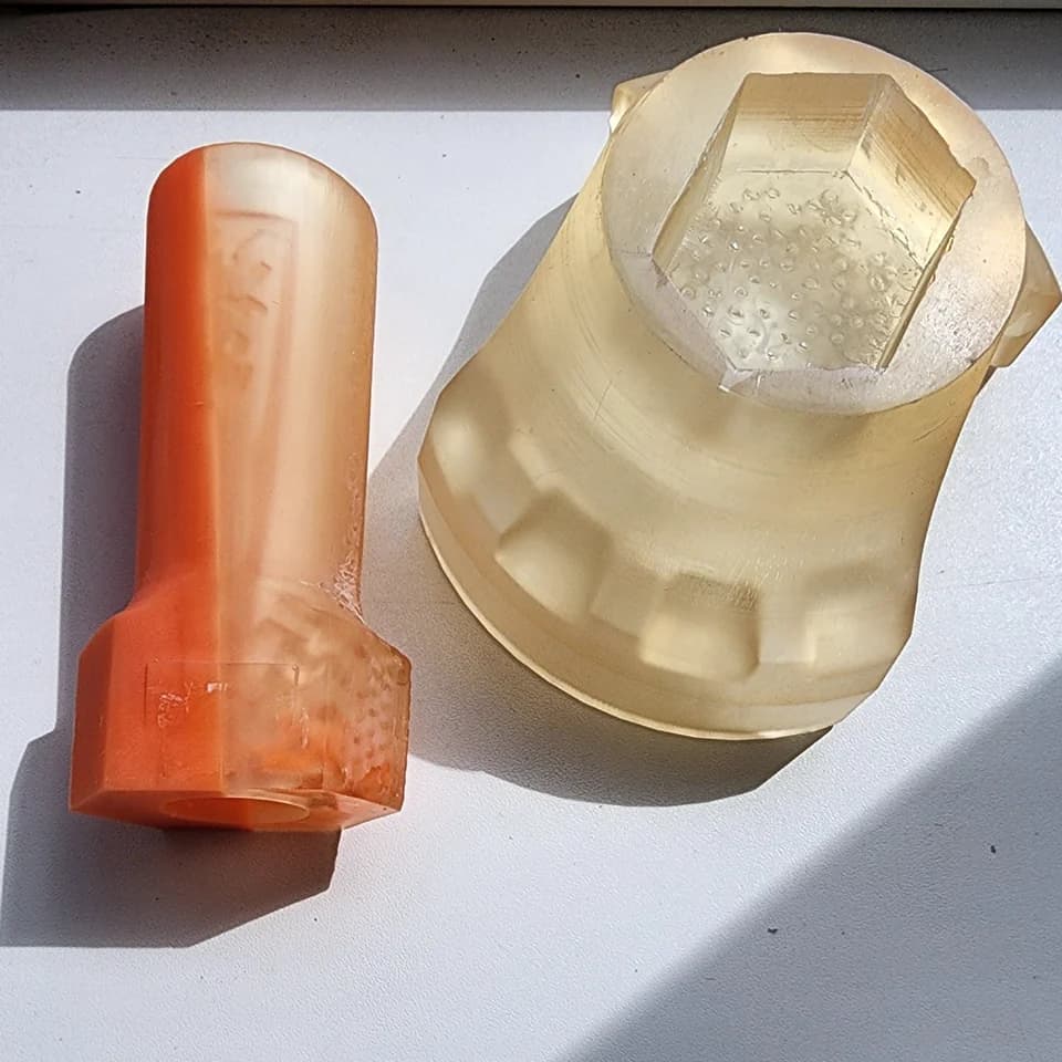 An orange cylindrical part and a wider pale part with a hexagonal recess on a white surface.