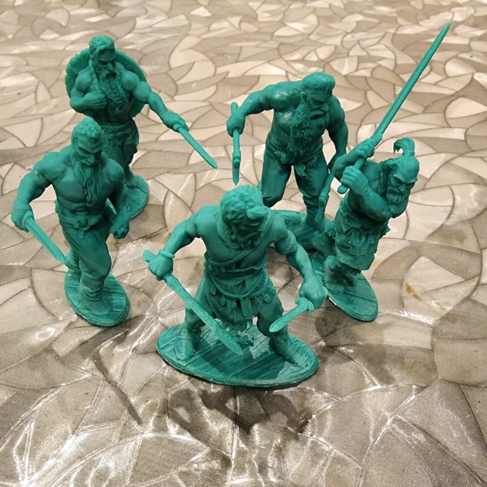 Five green warrior miniatures with swords and axes on textured bases, arranged on a work surface.