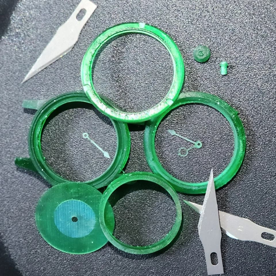 Green watch case rings, a circular insert and hands on a dark work surface.